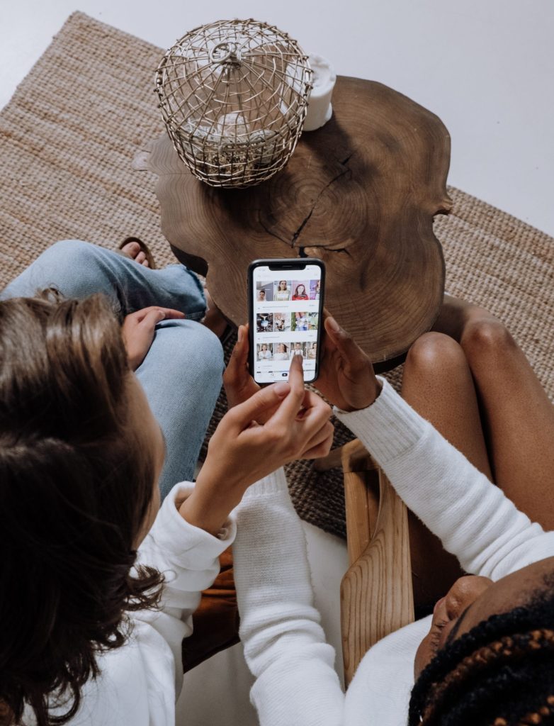 two girls scroll on phone on couch